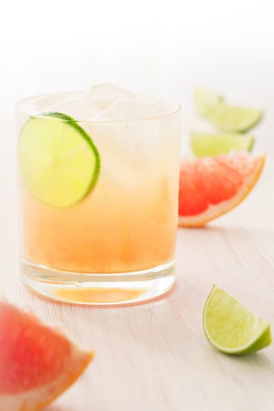 Paloma cocktail served with grapefruit and lime slices. White wooden background, high resolution